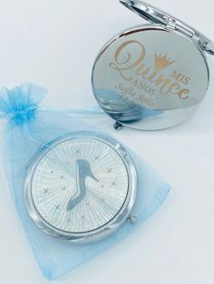 a compact mirror with a blue ribbon around it next to a small pocket watch on a white surface