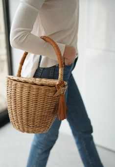 a woman carrying a wicker basket on her back while walking down the street in jeans