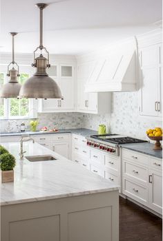 a large kitchen with white cabinets and marble counter tops, two pendant lights over the island