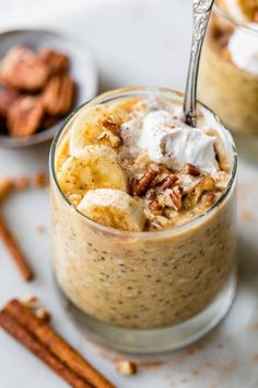 two glasses filled with pudding and whipped cream on top of a white table next to cinnamon sticks