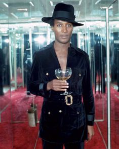 a man wearing a black hat and holding a wine glass in front of mirrored walls