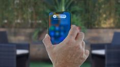 a person holding up an iphone in front of a table with chairs and plants on it