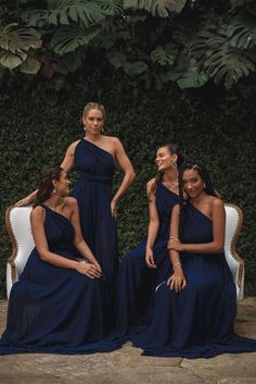 three women in blue dresses are sitting on a white chair and posing for the camera