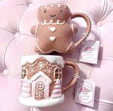 two mugs with gingerbread houses on them are sitting next to each other in front of a pink couch