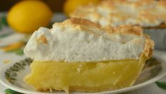 a slice of lemon meringue pie on a plate with another pie in the background