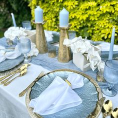 the table is set with blue and white plates, napkins, silverware and candles