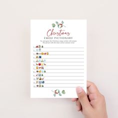 a hand holding up a christmas emojtionary printable with holly leaves on it