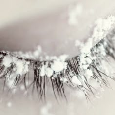 an extreme close up shot of the eyelashes of a woman's eye with snow flakes all over it