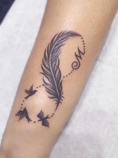 a black feather tattoo on the left forearm and foot, with an arrow in the middle