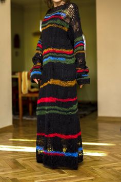 a woman standing in a room wearing a black dress with multicolored stripes on it