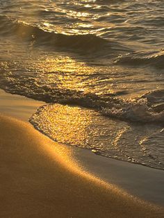 the sun shines on the water and sand at the beach as waves roll in