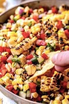 a hand is dipping corn into a bowl full of mexican street food with tortilla chips