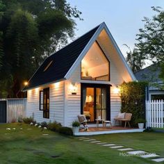 a small white house with a black roof and lights on it's front porch