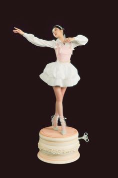 a woman in a white dress is standing on top of a cake with her arms outstretched