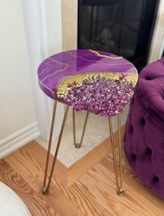 a purple and gold side table sitting on top of a wooden floor next to a fire place