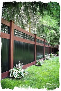 a wooden fence with green grass and trees in the background