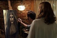 a woman is painting a man's face on an easel