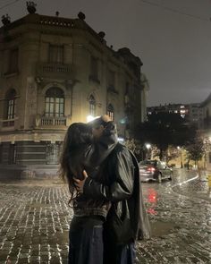 a man and woman kissing in front of a building on a wet street at night