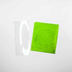 a piece of green paper sitting on top of a white wall next to a square shaped object