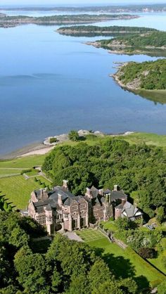 an aerial view of a large mansion in the middle of some trees with water behind it