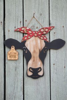 a cow with a red bow on it's head hanging from a wooden fence