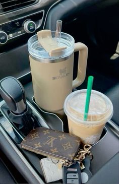 there are two drinks in the cup and a wallet on the car tray with keys