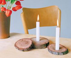 two white candles sitting on top of wooden slices next to a vase with red flowers