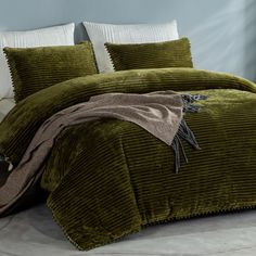 a bed with green bedspread and pillows on top of it in a room