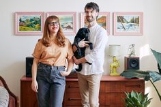 a man and woman standing next to each other holding a black dog in their hands