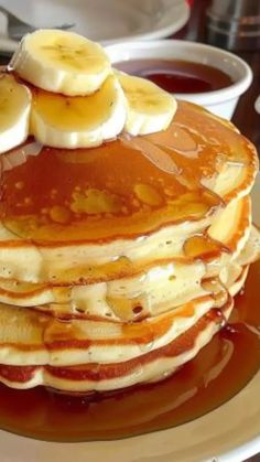 a stack of pancakes with bananas and syrup on a plate next to some chocolate sauce