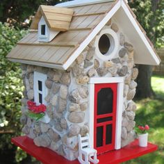 a bird house made out of rocks with a red door and window on the roof