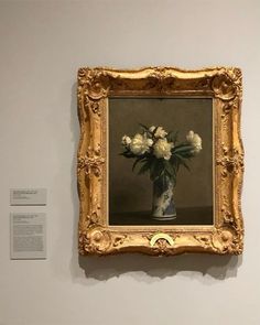 a vase with white flowers in it is on the wall next to a framed painting