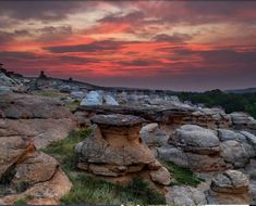 the sun is setting over some rocks and trees in the distance, with an orange sky behind them