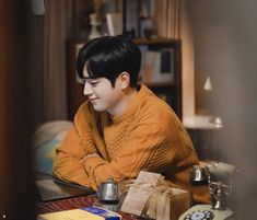 a young man sitting at a table in front of a laptop computer and coffee pot