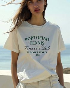 Grab your Vespa and your racket and get to the Portofino Tennis Club. Your retro passport to a stylish summer in Italia 1980. Ciao, bella! Unisex soft cotton crew neck t-shirt featuring a Portofino Tennis Club Italy 1980 graphic printed on the front. Fabrics: 100% cotton, 6.1 oz Made in: LA Models wearing S/M Summer Tennis Tops With Short Sleeves, Summer Cotton Tennis Tops, Summer Short Sleeve Tennis Tops, Short Sleeve Summer Tennis Tops, Short Sleeve Tennis Tops For Summer, Cotton Tennis Tops For Summer, Casual Tennis Tops For Spring, Vintage Printed T-shirt For Summer, Summer Crew Neck T-shirt For Leisure