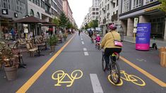 a person riding a bike down a street with yellow markings painted on the road and buildings in the background