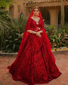 a woman in a red wedding dress standing on a brick floor with greenery behind her