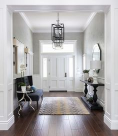 a hallway with white walls, wood floors and a chandelier hanging from the ceiling