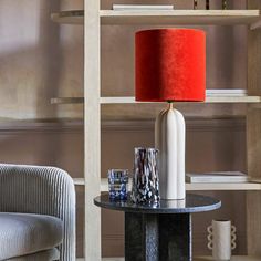 a table with a lamp on it next to a chair and bookshelf in the background