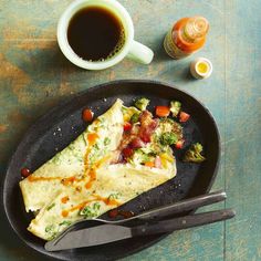 an omelet with broccoli and tomatoes on a plate next to a cup of coffee