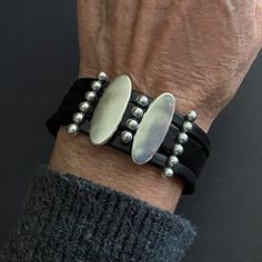 a man's hand wearing a black leather bracelet with silver beads and oval discs