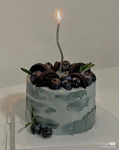 a birthday cake with blueberries and cookies on it is lit by a single candle