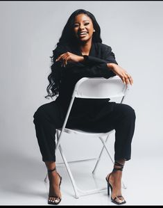 a woman sitting in a white chair with her arms crossed and smiling at the camera