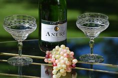 a bottle of wine and two glasses on a glass table with grass in the background