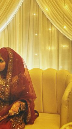 a woman sitting on top of a couch in front of a window wearing a red and gold dress