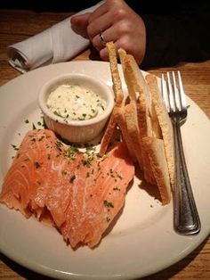 a white plate topped with fish and bread next to a bowl of dip on top of it