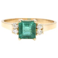 an emerald and diamond ring with three diamonds on the side, set in yellow gold