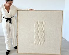 a woman standing next to a white wall holding up a piece of art on display