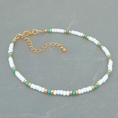 a white beaded bracelet with gold accents on a gray surface, the beads are green and white