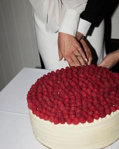 two people are cutting into a cake with raspberries on the top and bottom